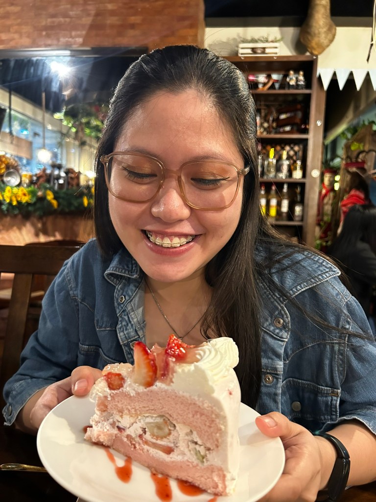 a smiling woman holding a plate with a slice of strawberry shortcake